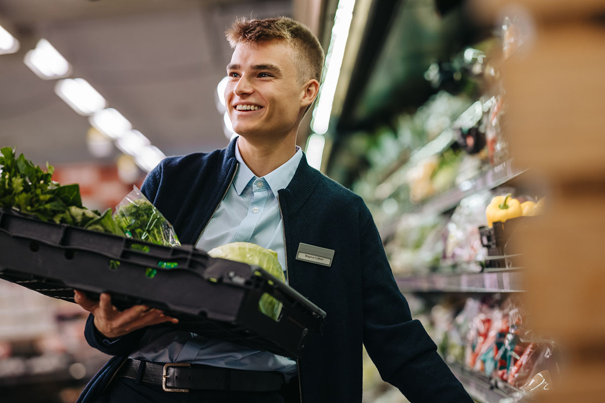 Junger Mann, der im Supermarkt Gemüse einsortiert