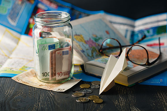 Geldscheine in einem Glas auf einer Wanderkarte und Brille mit Buch